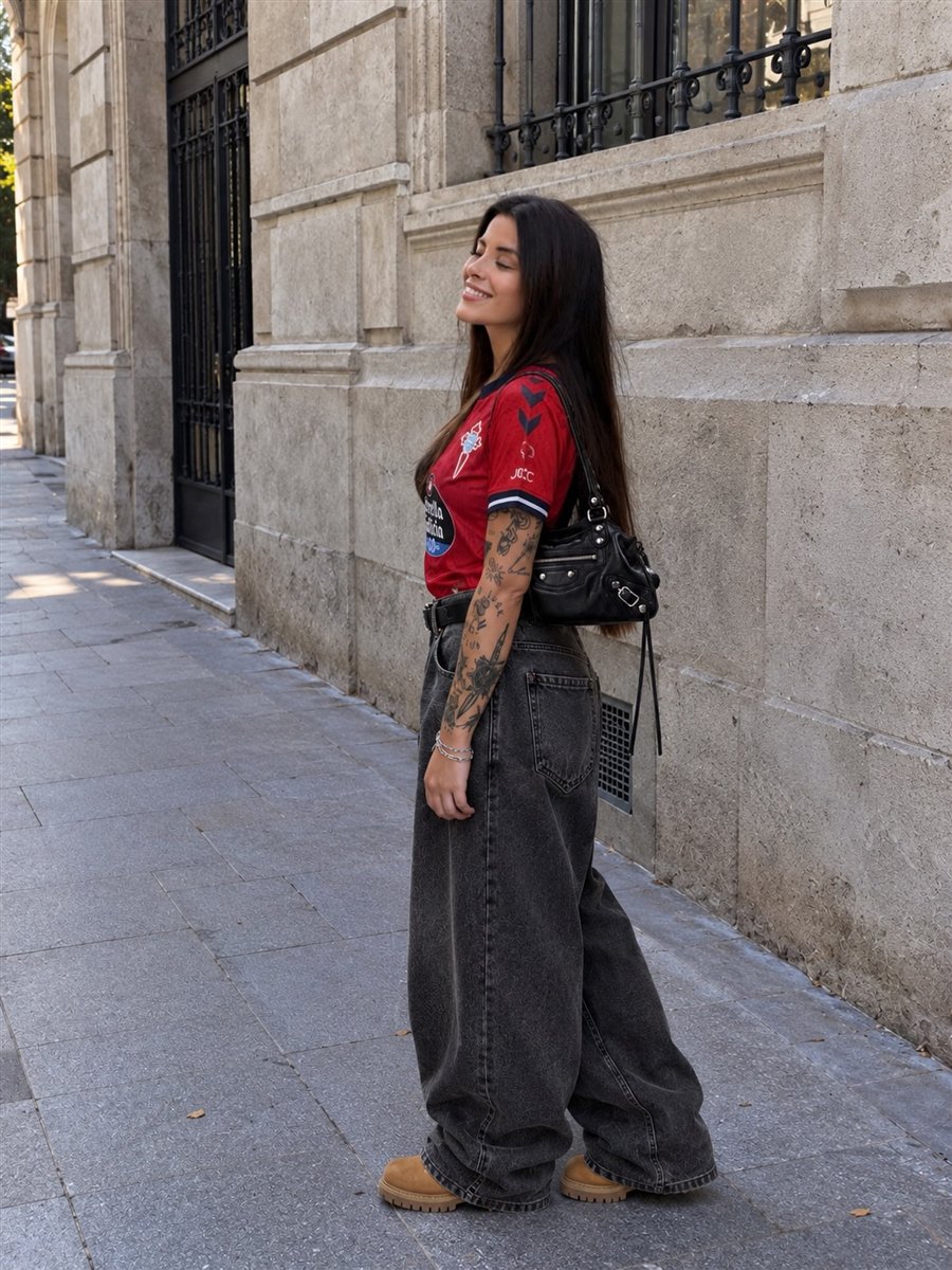 Outfit urbano con camiseta roja de fútbol, vaqueros anchos negros, botas y bolso negro